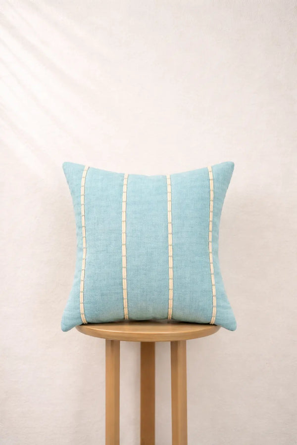 Light blue pillow with gold stripes on a wooden stool against a beige background