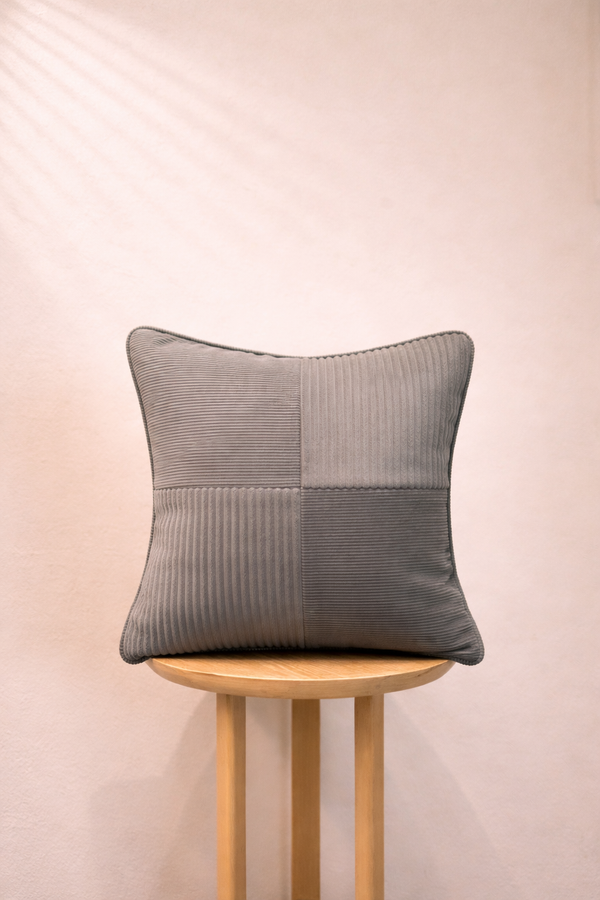 Gray patchwork pillow on a wooden stool against a beige background