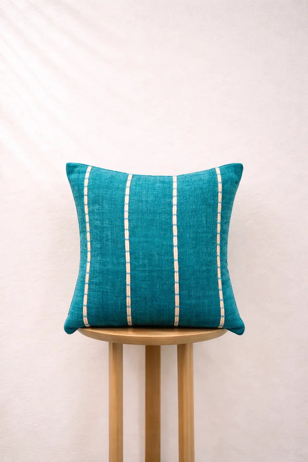 Lagoon pillow with white stripes on a wooden stool against a light background