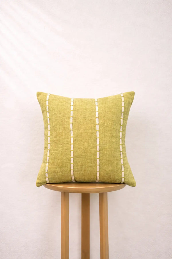 Olive gold pillow with white stripes on a wooden stool against a white background