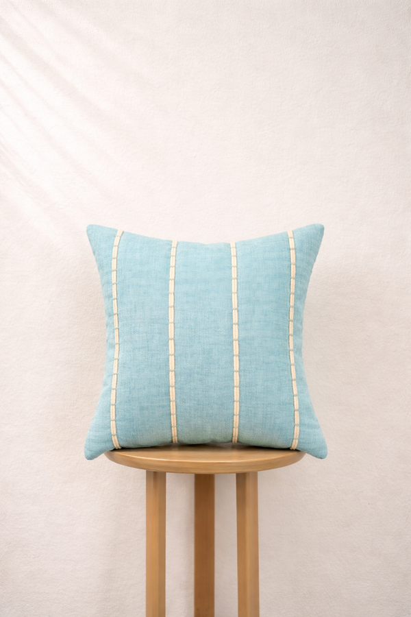 Light blue pillow with gold stripes on a wooden stool against a beige background