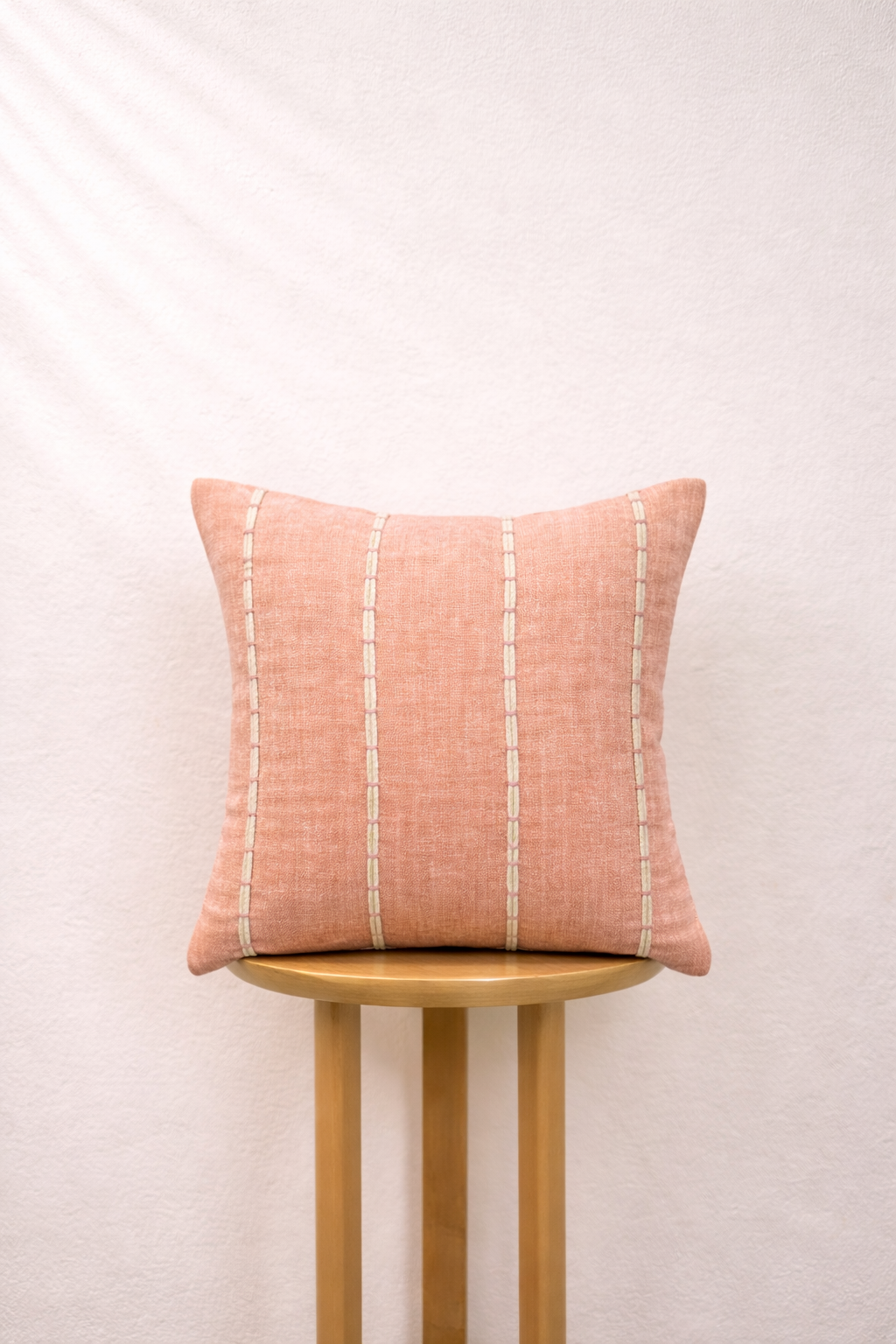 Blush cushion with white stripes on a wooden stool against a light background