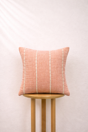 Blush cushion with white stripes on a wooden stool against a light background