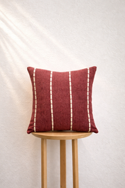 Red pillow with white stripes on a wooden stool against a white background