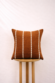 Burnt Caramel pillow with white stripes on a wooden stool against a light background