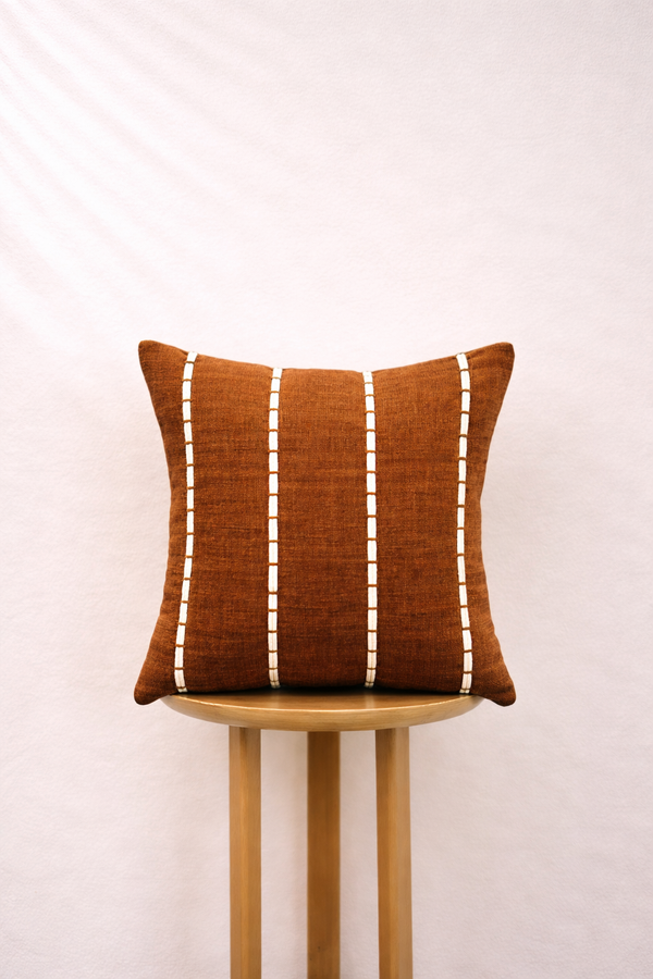 Burnt Caramel pillow with white stripes on a wooden stool against a light background