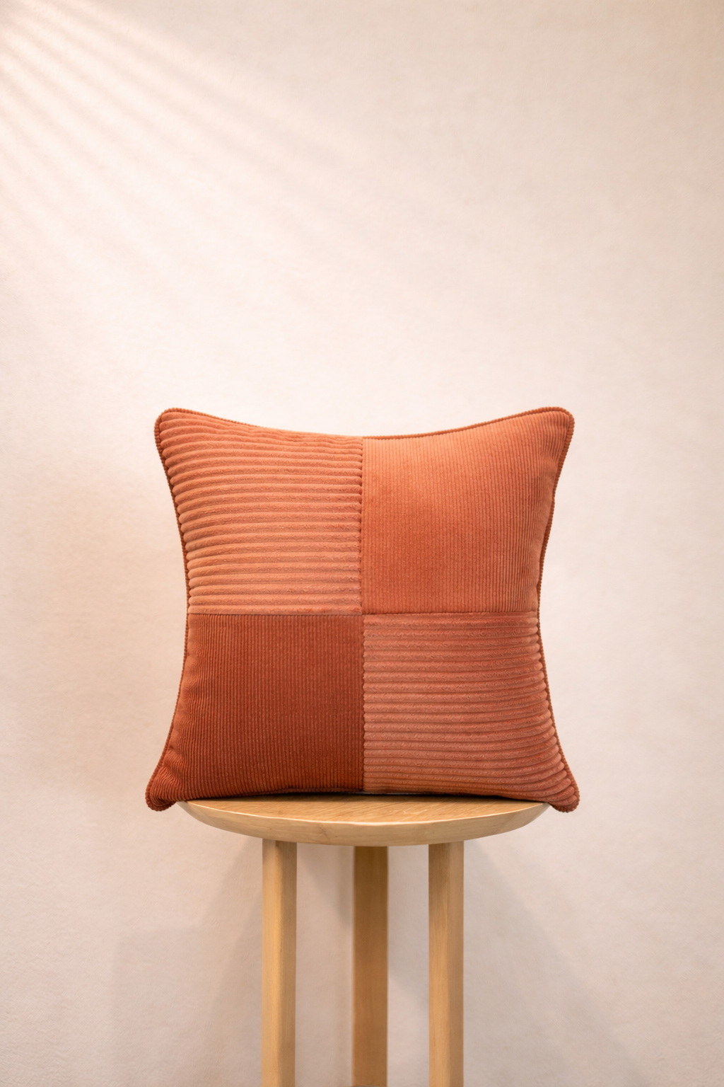 Burnt Terracotta Cushion with a patchwork design on a wooden stool against a beige background