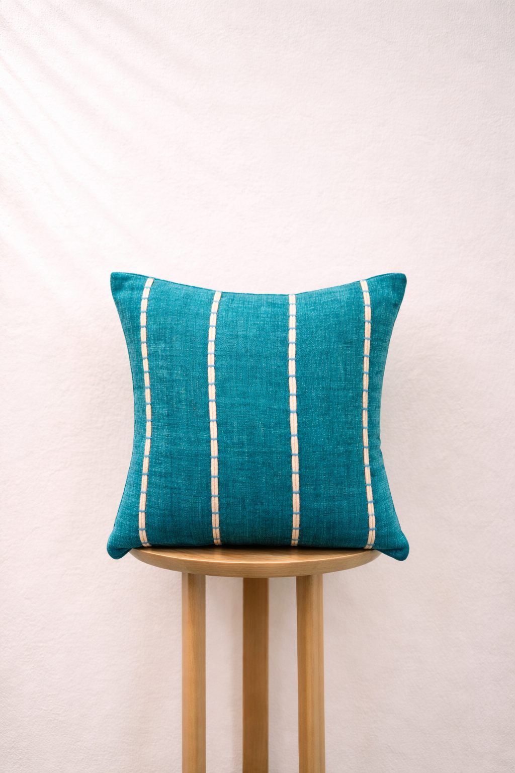 Lagoon pillow with white stripes on a wooden stool against a light background