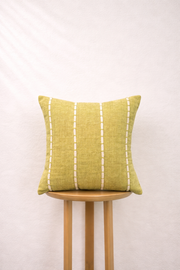 Olive gold pillow with white stripes on a wooden stool against a white background