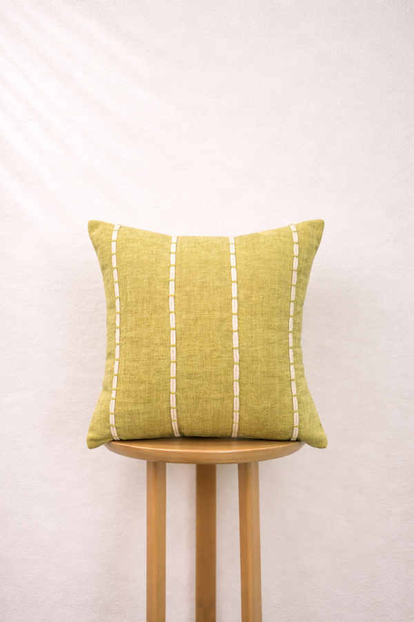 Olive gold pillow with white stripes on a wooden stool against a white background