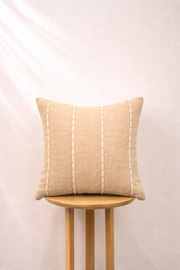 Sand pillow with white stitching on a wooden stool against a light pink background